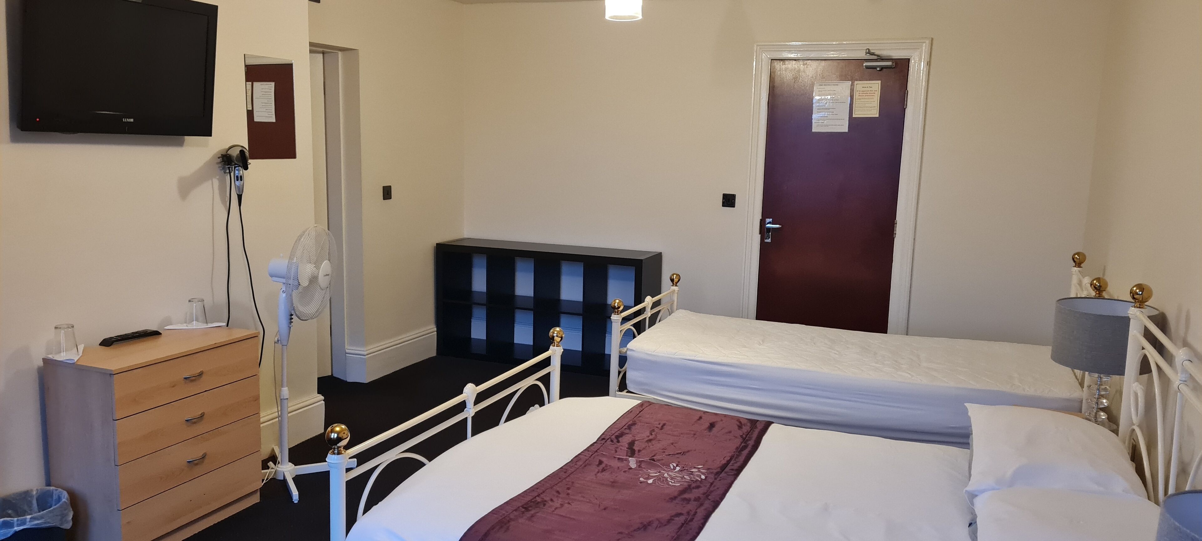 A hotel room with a bed, bedside table, dresser, and a television mounted on the wall.
