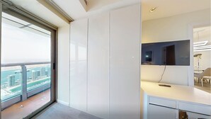 A modern hotel room with a large window offering a city view, a flat-screen TV mounted on the wall, and a minimalist desk area. - Luxurious 1 Bedroom-High floor-Sea view and Balcony (Dubai)