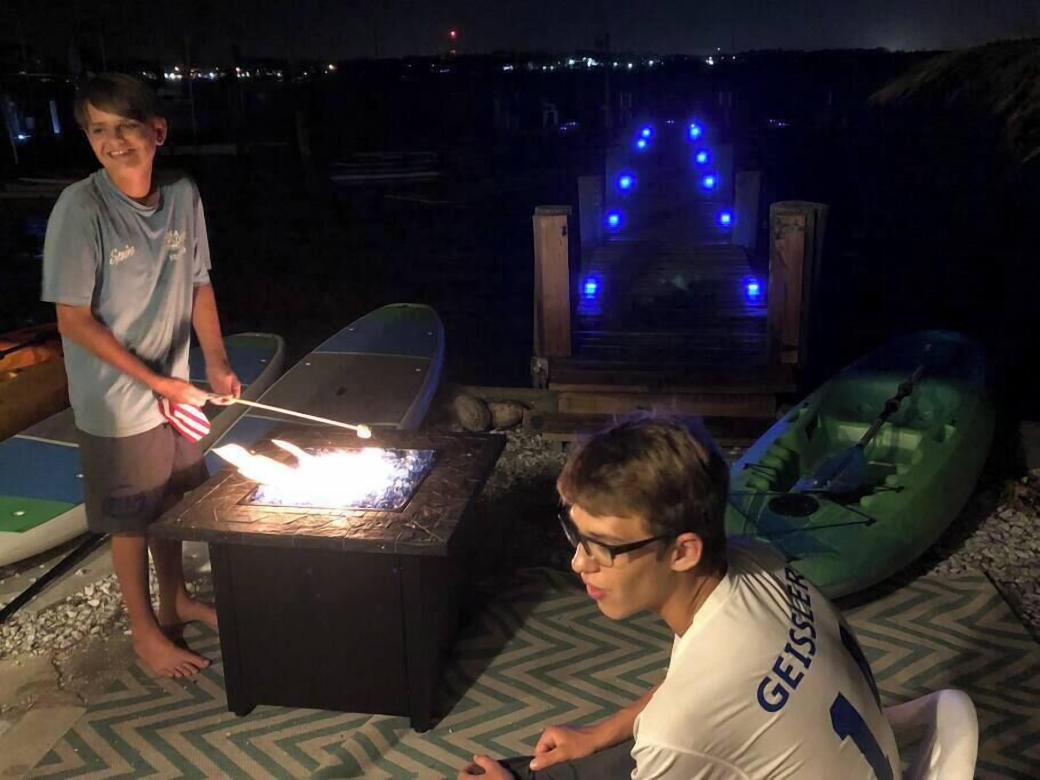 Two people near a fire pit with boats in the background.