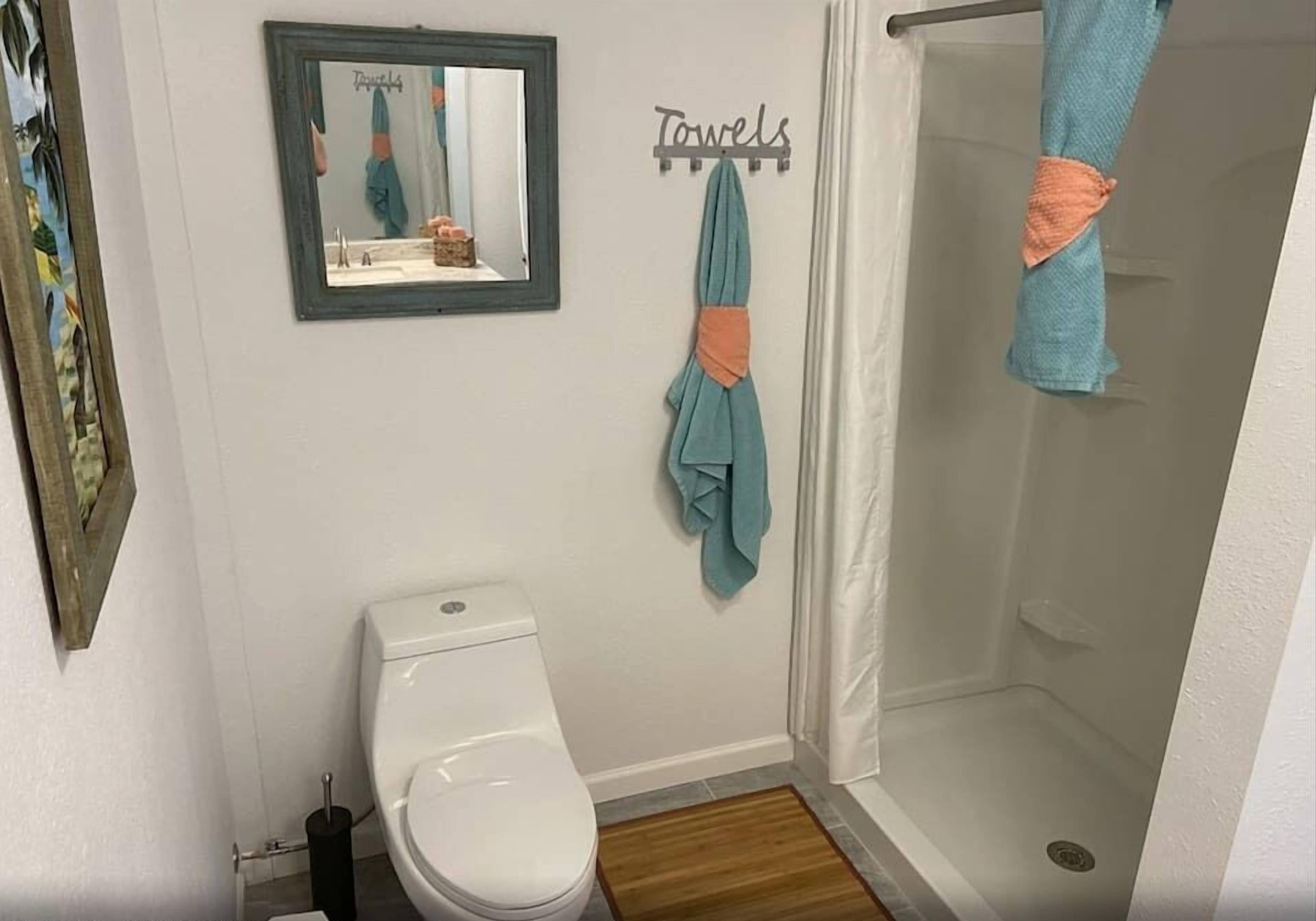 A bathroom with a toilet, a shower, a towel rack with towels, and a mirror.