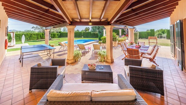 Ein Terrassenbereich im Freien mit Rattanmöbeln, einem Pool und einer überdachten Lounge-Ecke.