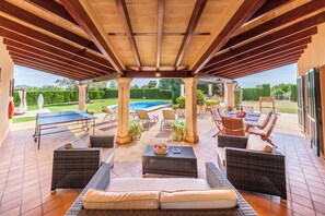 Un espace extérieur aménagé en terrasse, avec des meubles en osier, une piscine et un coin salon abrité.