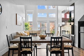 A modern dining area with a wooden table, chairs, and a sofa. - 3BR | Garage | DT Views | Central | Lux Townhome (Calgary)