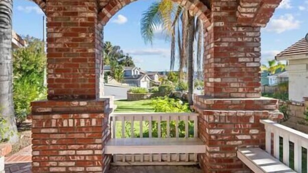 A brick archway with a white railing, leading to a view of a residential area with houses and greenery. - Big Red Brick Home near Six Flags Magic Mountain (Castaic)