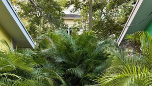 A small outdoor seating area with a white table and two white chairs, surrounded by lush green foliage and a gravel ground. - Stylish Garden Retreat in Coconut Grove - Green (Coral Gables)