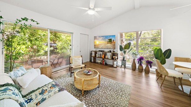 A spacious living room with a ceiling fan, large windows, a round coffee table, and a bookshelf. - Stylish Garden Retreat in Coconut Grove - Green (Coral Gables)