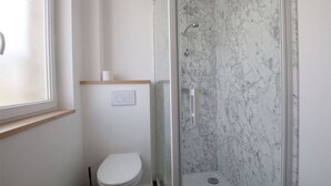 Un baño con inodoro, ducha con puerta de vidrio y pared de mármol.