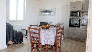 Un comedor con una mesa lista para cuatro personas, un frutero sobre la mesa, y una cocina con microondas y horno al fondo.