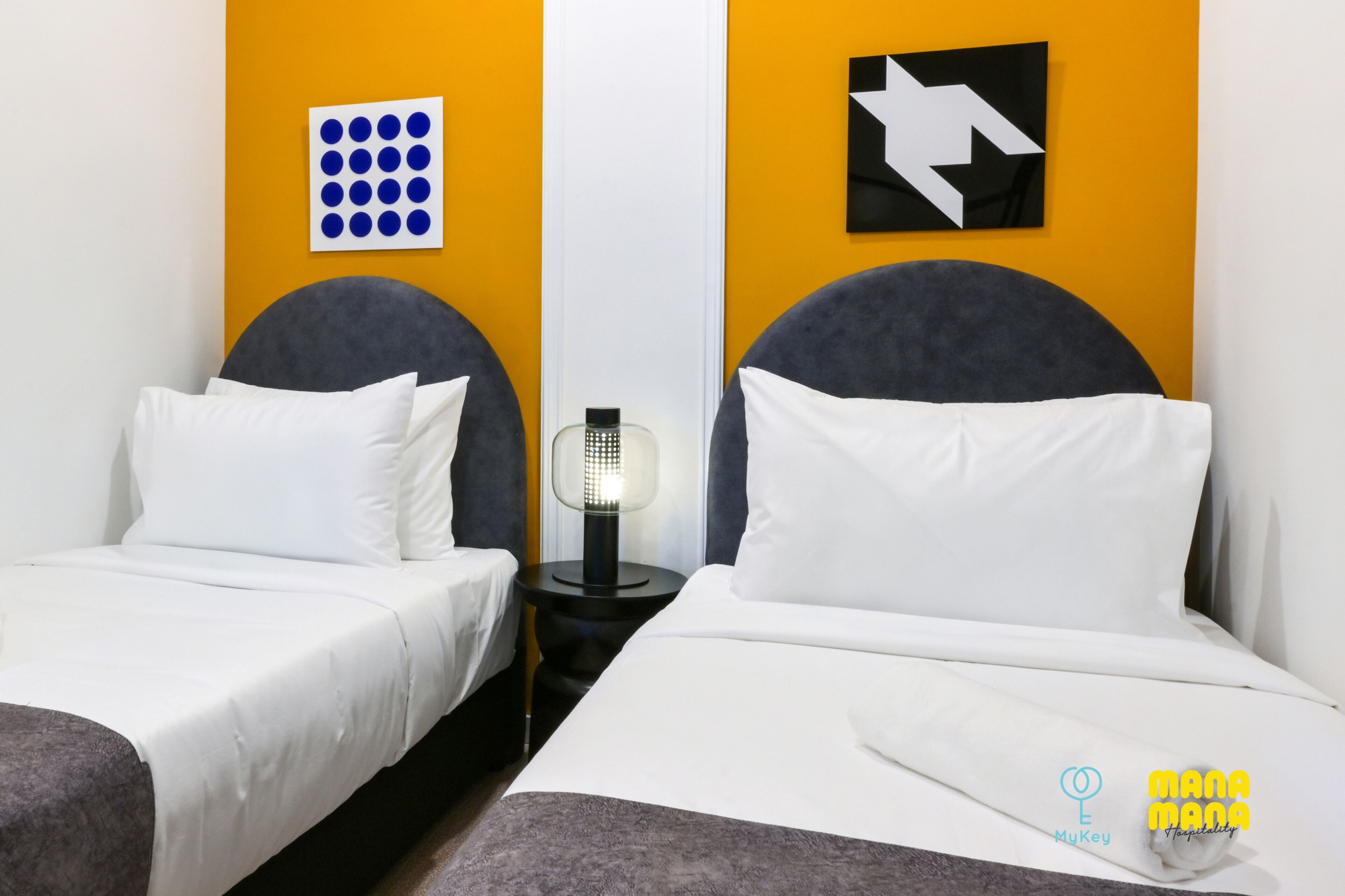 A hotel room with two beds, a nightstand with a lamp, and artwork on the walls.