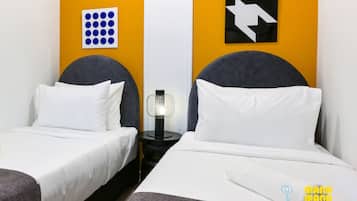 A hotel room with two beds, a nightstand with a lamp, and artwork on the walls.