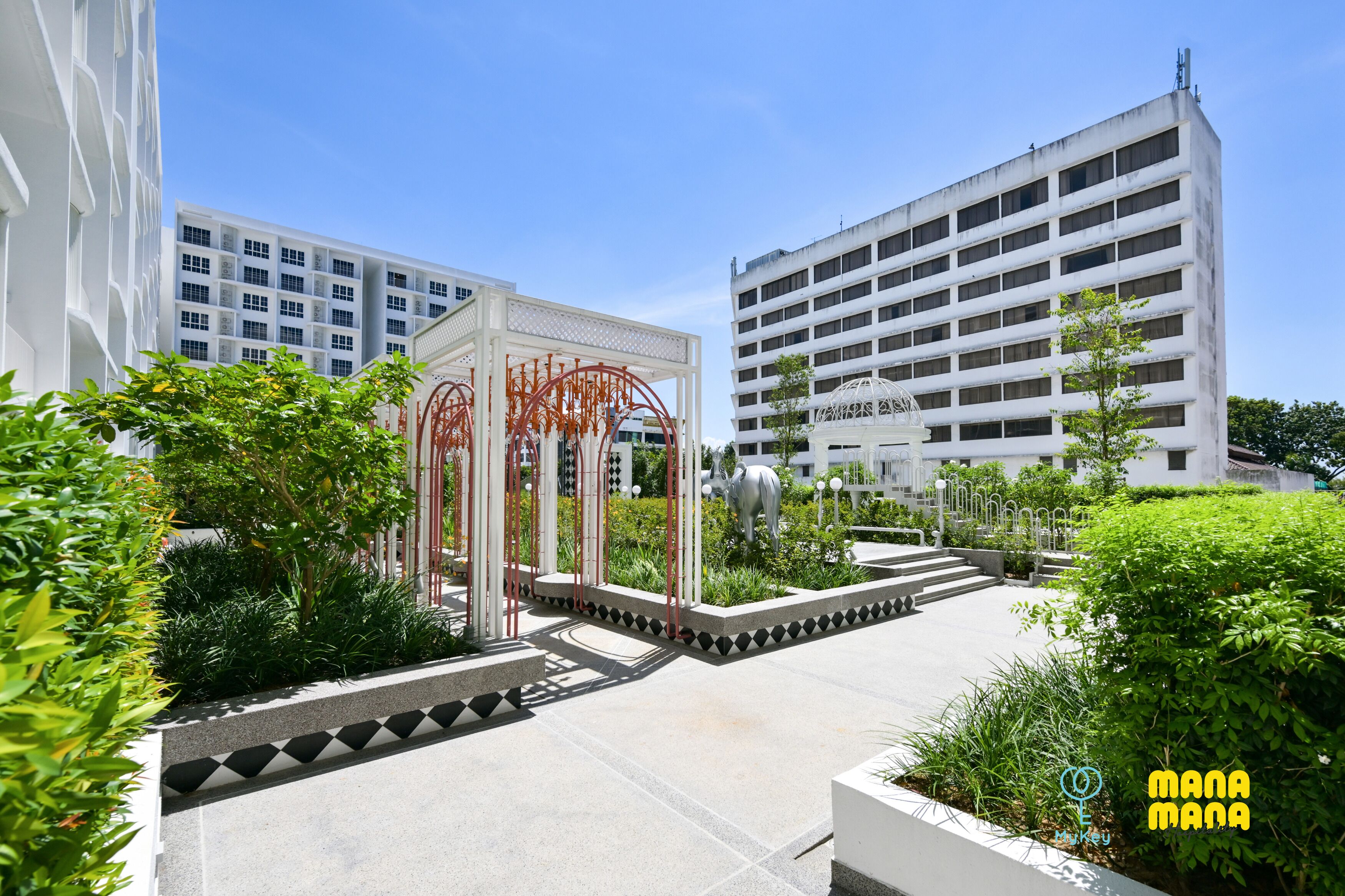 A modern building with a central courtyard featuring a metal sculpture, surrounded by greenery and a clear sky.