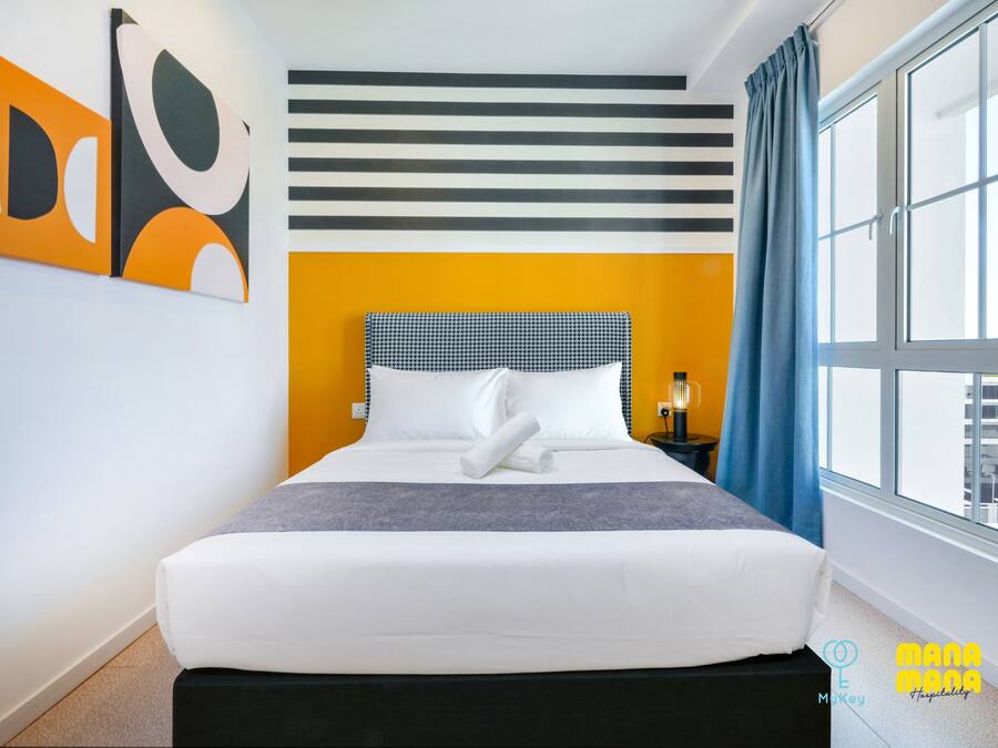 A hotel room with a large bed, a striped wall, and a window with curtains.