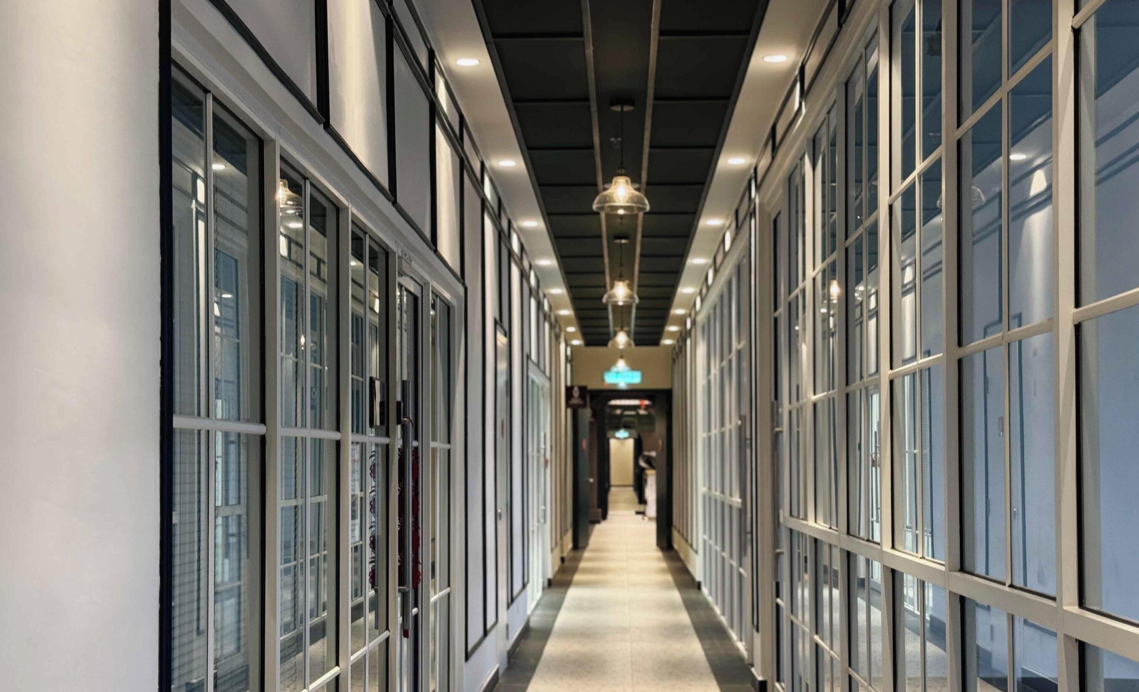A corridor with glass doors, overhead lighting, and a visible sign.