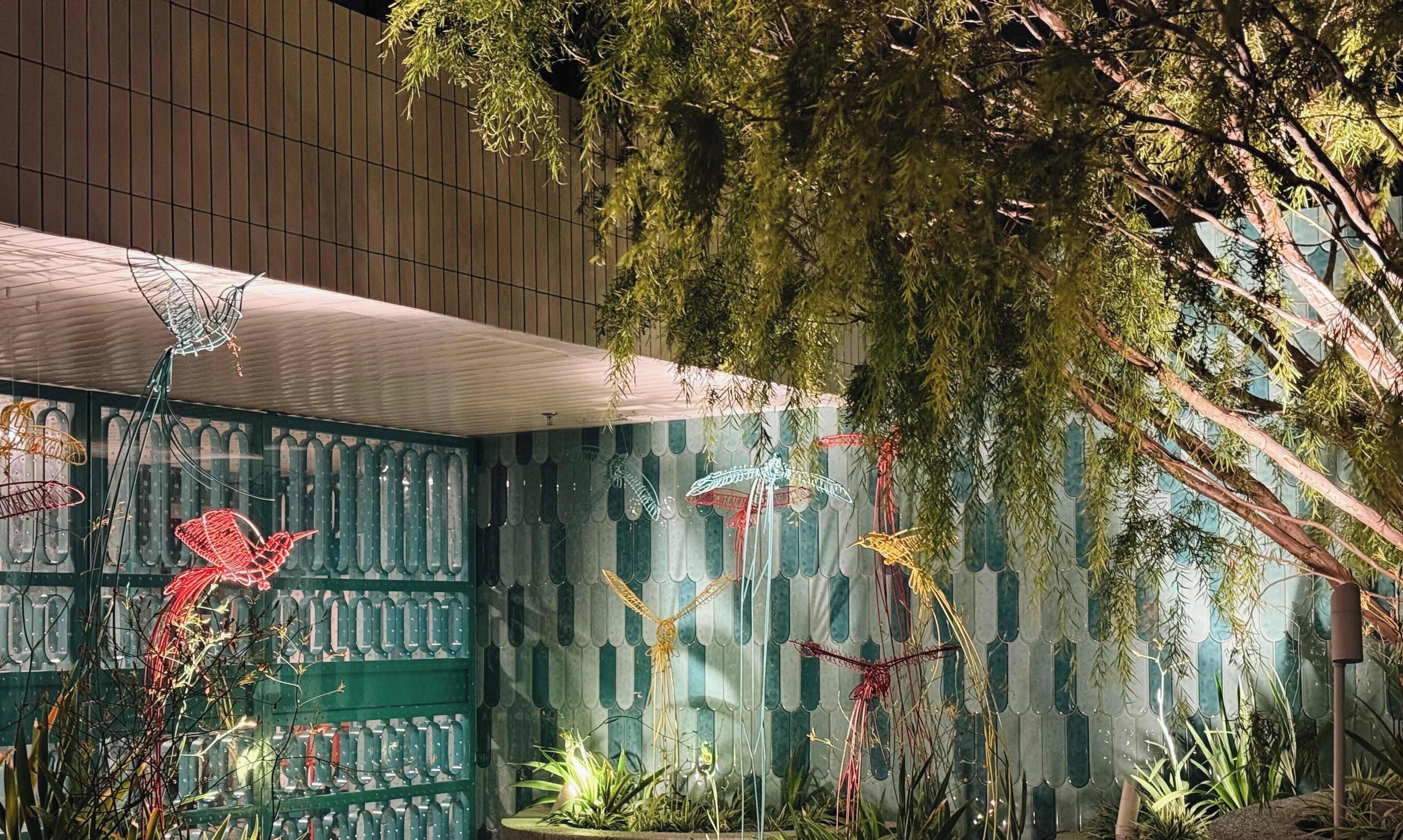 Una habitación con pared de diseño verde, una planta colgante y una verja metálica decorativa.