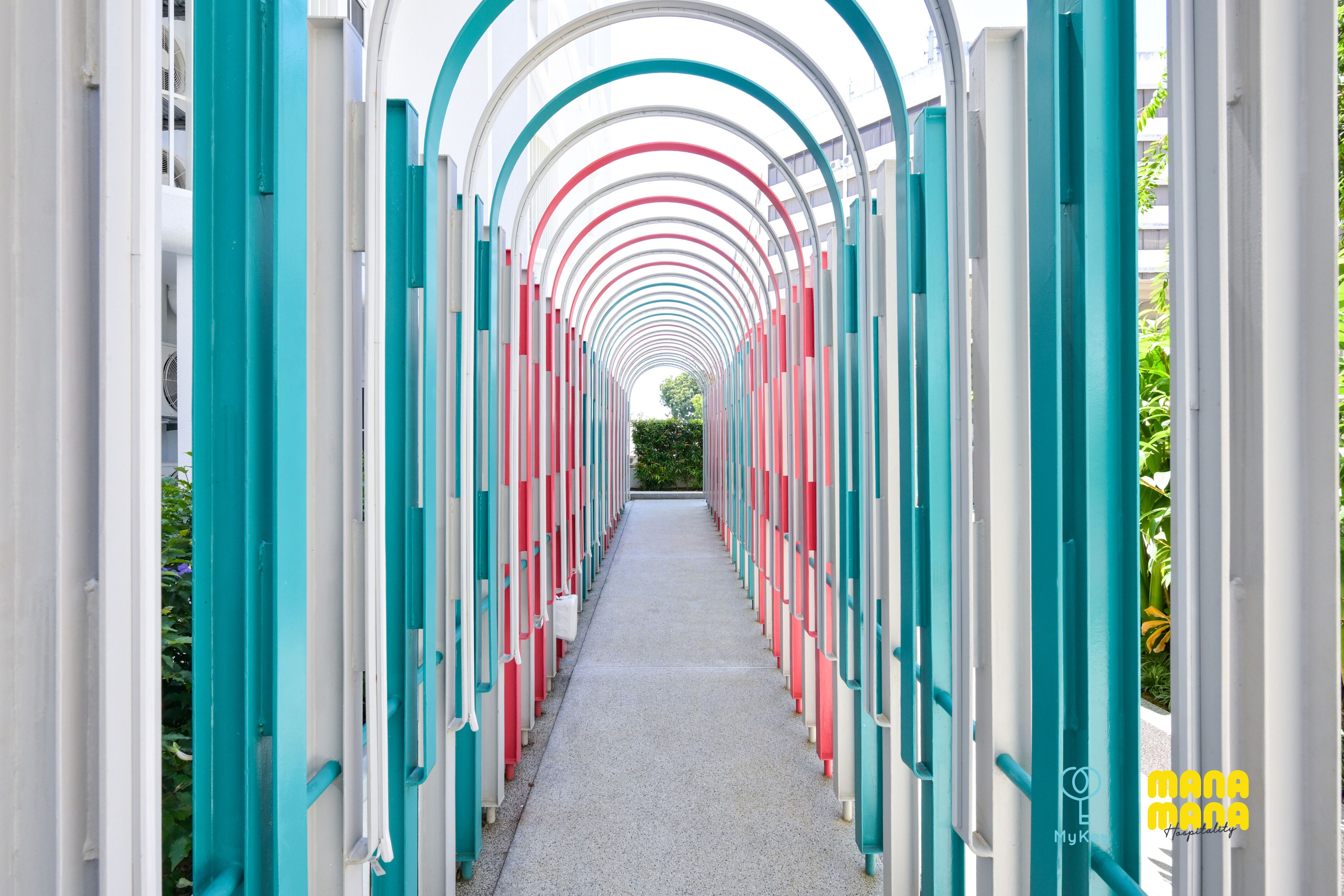 A corridor with a repeating pattern of arches and columns, leading to a distant green area.