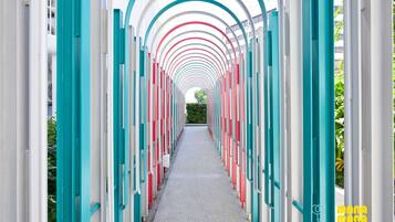 A corridor with a repeating pattern of arches and columns, leading to a distant green area.