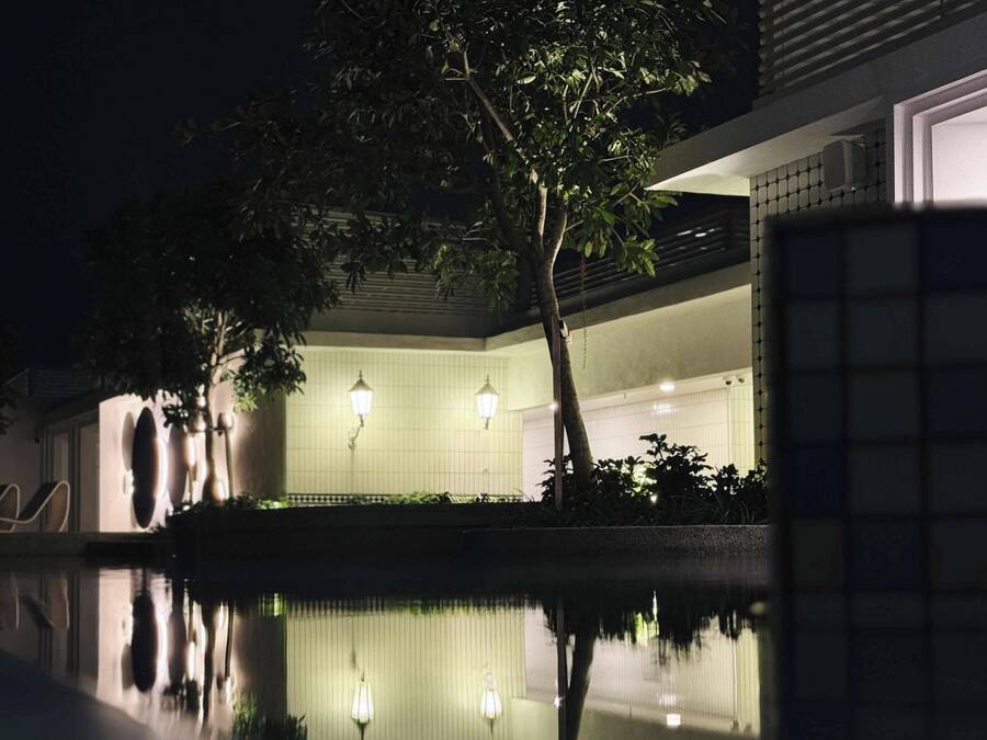 A modern building with a pool, trees, and two lit wall lamps.
