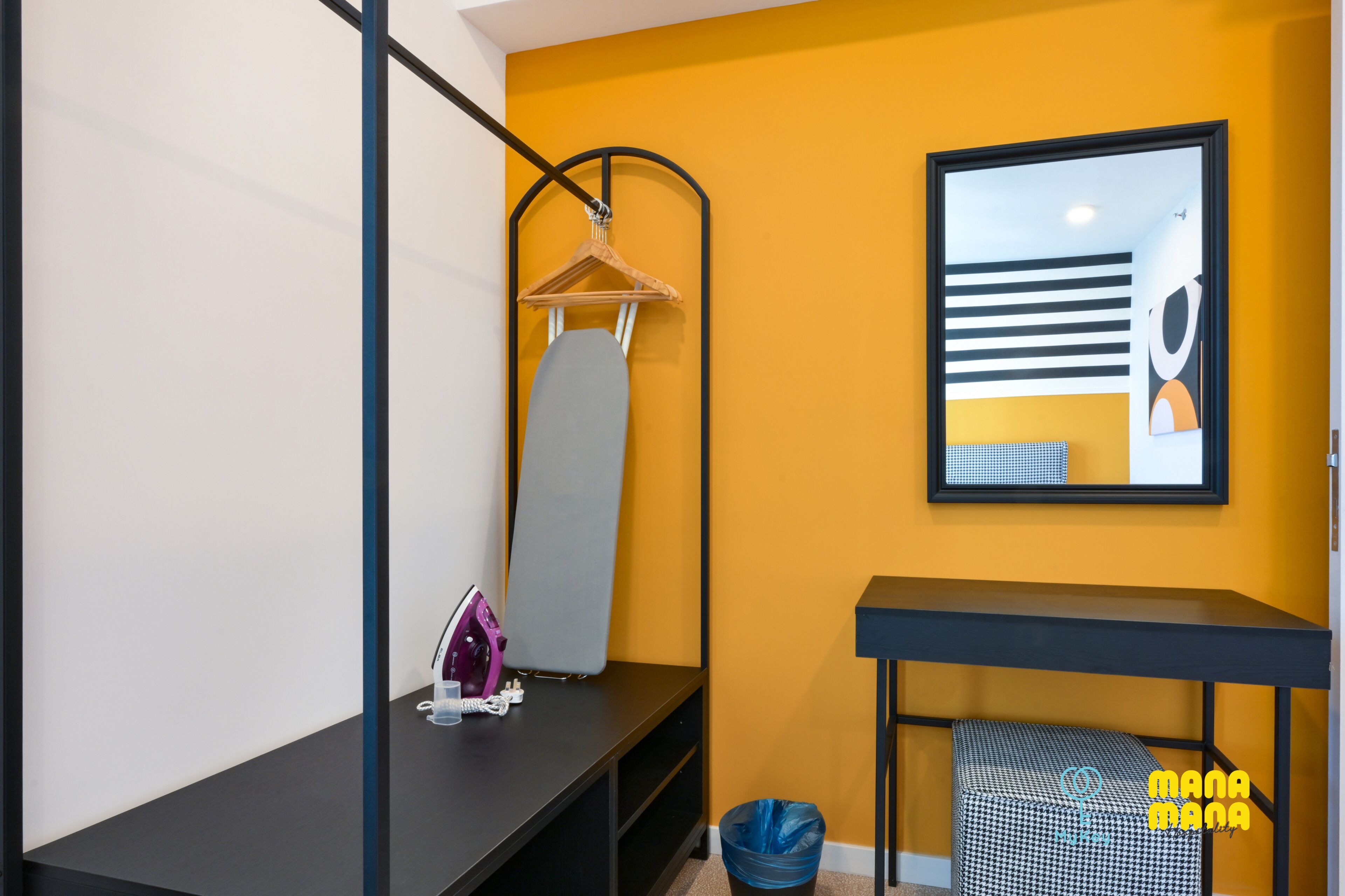 A modern bathroom with a yellow accent wall, a black vanity, a hanging iron, and a trash bin.