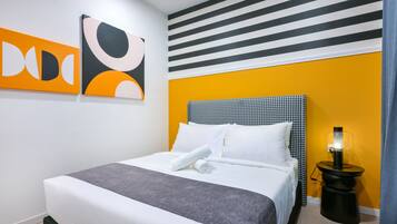 A neatly made bed with white linens and a grey throw, a black and white houndstooth headboard, and a black bedside table with a lamp.