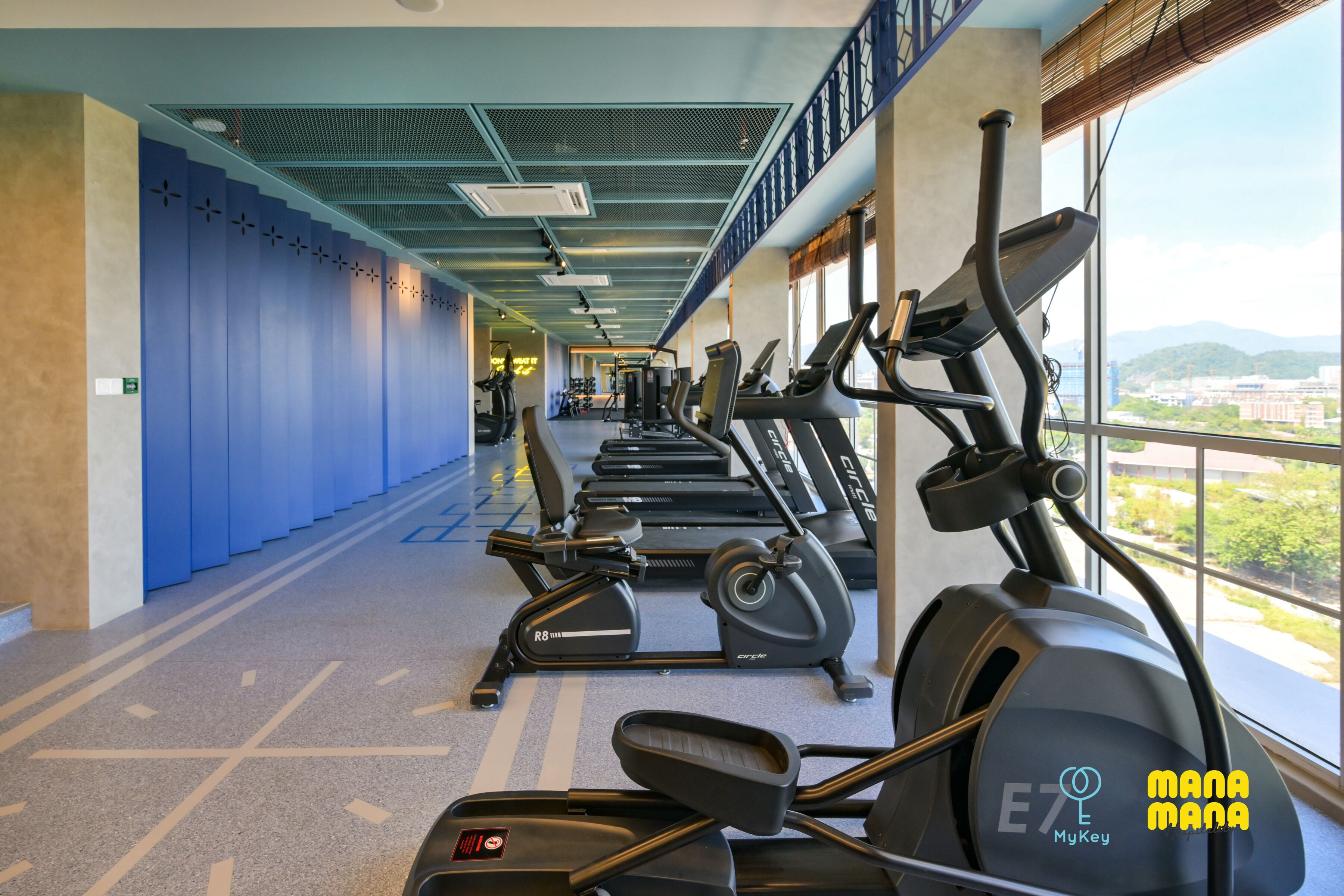 A gym with treadmills and elliptical machines, a blue wall, and a window with a city view.
