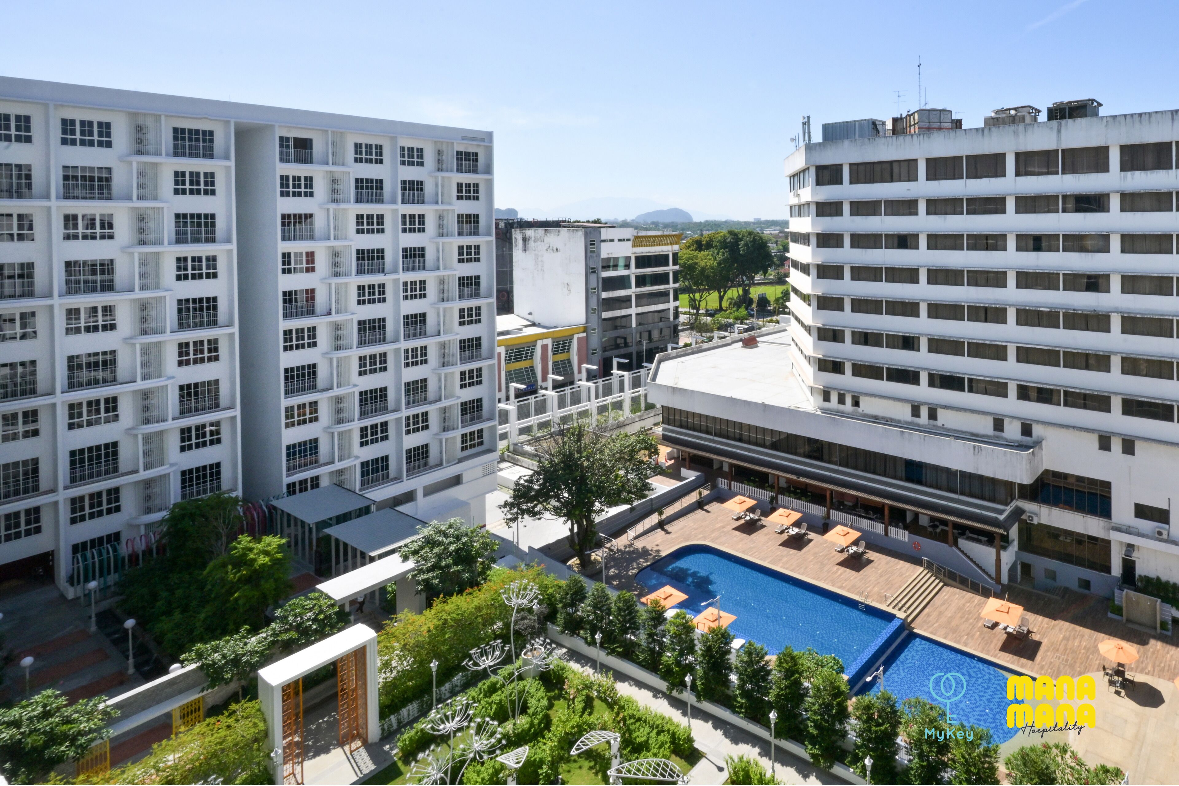A modern hotel with multiple floors, a rooftop pool area, and surrounding greenery.