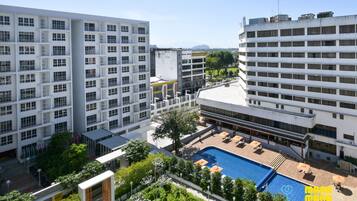 A modern hotel with multiple floors, a rooftop pool area, and surrounding greenery.