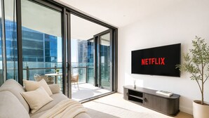 Un salón moderno con sofá, televisor montado en la pared, planta en maceta y balcón con mesa y sillas.
