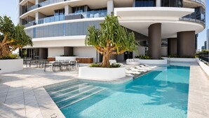 Un área de piscina moderna de hotel con una piscina cristalina, sillas de descanso y un comedor.