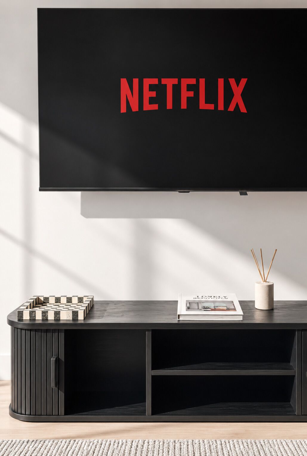 A modern living room with a flat-screen TV displaying 'NETFLIX' in red letters, a chessboard, a magazine, and a candle holder on a dark wooden console.