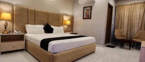 A modern hotel room with a large bed, a ceiling fan, and a seating area with two chairs.