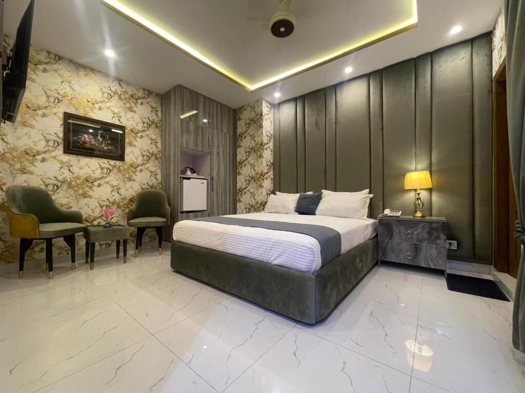 A modern bedroom with a large bed, two armchairs, a nightstand, and a wall-mounted TV.