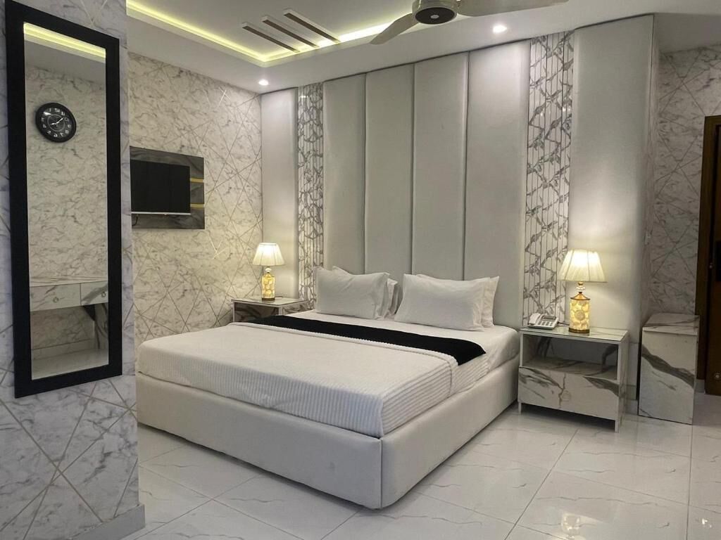A modern bedroom with a large bed, a TV mounted on the wall, and two bedside tables with lamps.