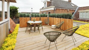 A wooden deck with a table and chairs, a brick house in the background, and a wooden fence. - Luxury Apartment in the Heart of Dokkum (Dokkum)