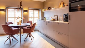 A modern kitchen with a dining area, featuring a round table with chairs, a built-in oven, and a refrigerator. - Luxury Apartment in the Heart of Dokkum (Dokkum)