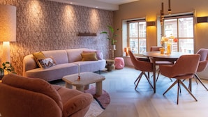 A modern living room with a stone wall, a sofa, a dining table with chairs, and a small side table with a candle. - Luxury Apartment in the Heart of Dokkum (Dokkum)