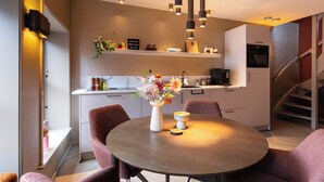 A modern kitchen with a dining area, featuring a round table, chairs, pendant lights, and a staircase. - Luxury Apartment in the Heart of Dokkum (Dokkum)