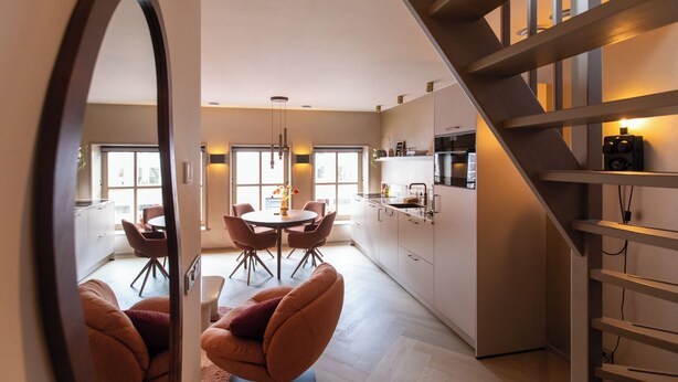 A modern kitchen with a central island, dining area with chairs, and a staircase. - Luxury Apartment in the Heart of Dokkum (Dokkum)