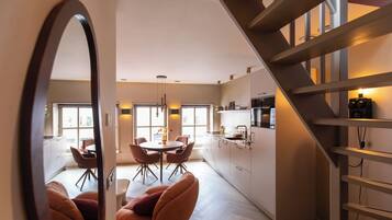 A modern kitchen with a central island, dining area with chairs, and a staircase.