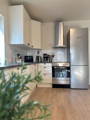 A modern kitchen with white cabinets, a stainless steel refrigerator, a built-in oven, and a microwave. - Modern apartment with terrace - SOLIS (Tromsø)