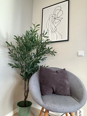 A room with a grey armchair, a green plant in a pot, and a framed abstract artwork on the wall. - Modern apartment with terrace - SOLIS (Tromsø)