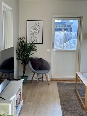 A living room with a television, a chair, a plant, and a door with a view of a snowy landscape. - Modern apartment with terrace - SOLIS (Tromsø)