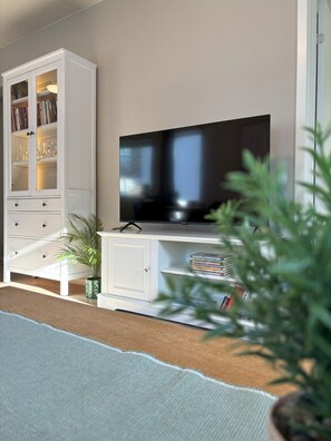 A living room with a flat-screen TV, a white cabinet with glass doors, and a small plant. - Modern apartment with terrace - SOLIS (Tromsø)