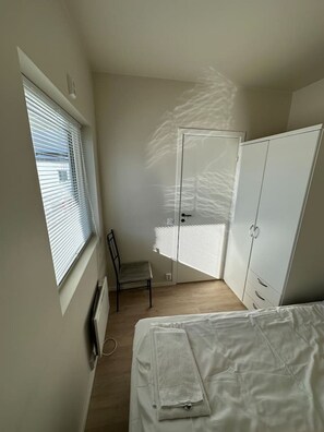 A small, sparsely furnished room with a single bed, a chair, a radiator, a window with blinds, and a wardrobe. - Modern apartment with terrace - SOLIS (Tromsø)