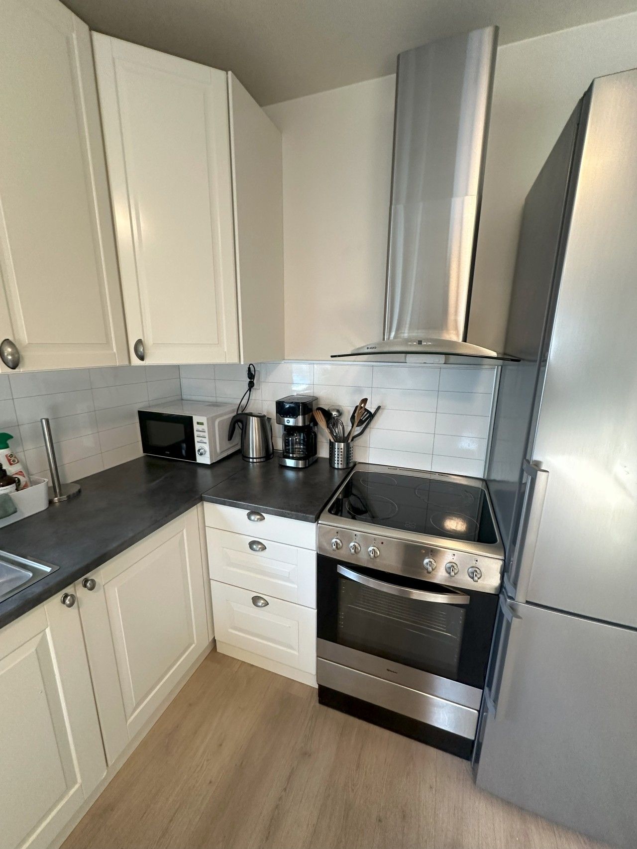 Een functionele keuken met witte kastjes, een zwart aanrecht, een roestvrijstalen fornuis en een inbouwoven.