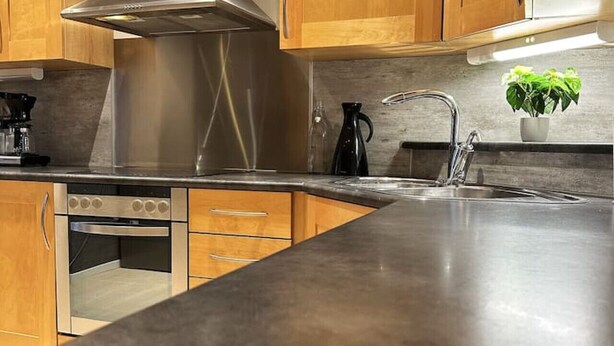 A modern kitchen with wooden cabinets, stainless steel appliances, and a granite countertop. - Sentrumsnær leilighet med 5 soverom - Montis (Tromsø)