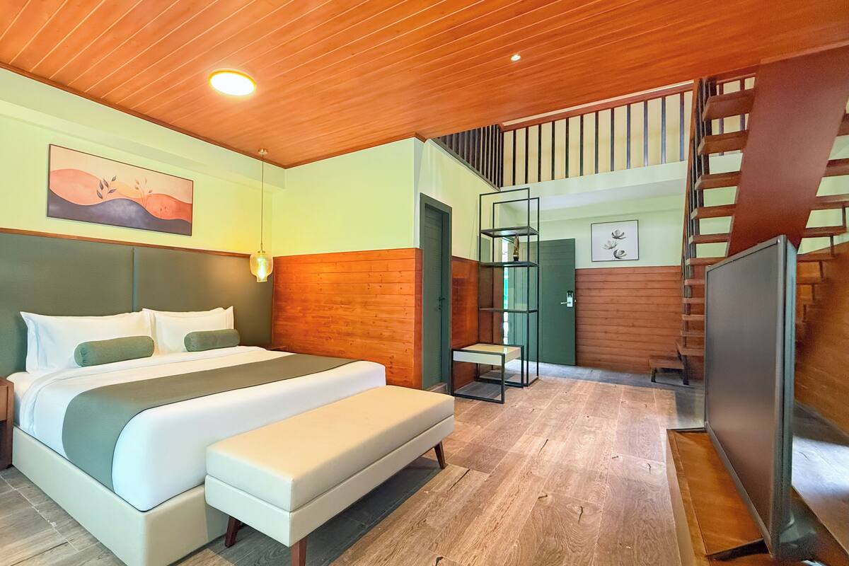 Ein modernes Hotelzimmer mit einem großen Bett, einem Nachttisch mit Lampe, einem Holz-Kopfteil, einer Treppe und Blick ins Freie.