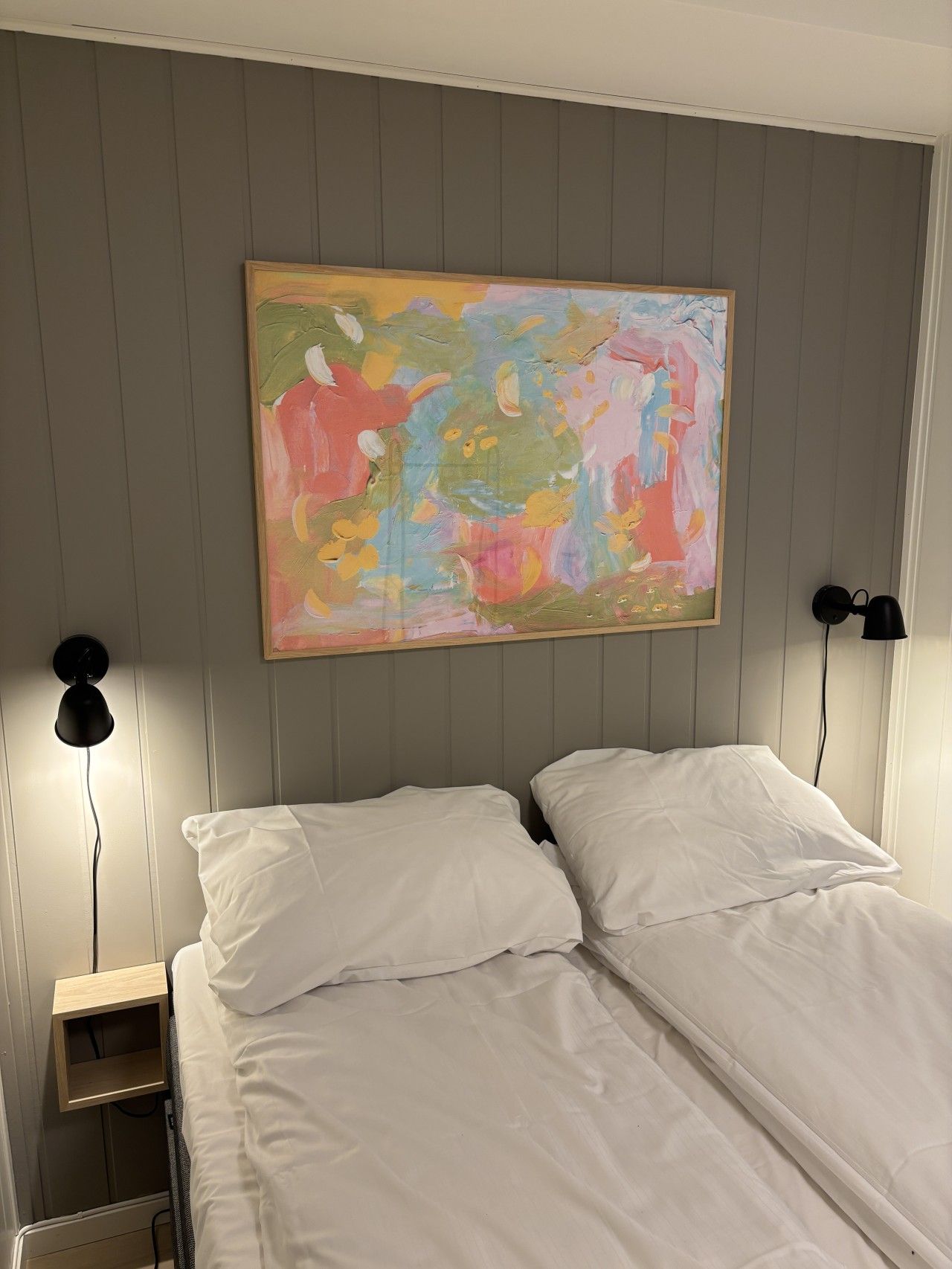 Een kamer met een bed, twee bedlampjes en een kleurrijk abstract schilderij aan de muur.