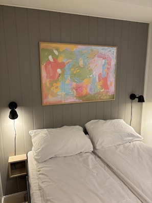 Huoneessa on sänky, kaksi yöpöytälamppua ja seinällä värikäs abstrakti maalaus.