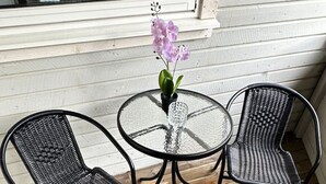 Un tavolo rotondo in vetro con un vaso di fiori, affiancato da due sedie in vimini.