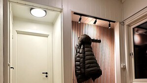 A hallway with a white door, a bench with a coat rack, and a wooden slatted wall. - Sentrumsnær leilighet med 4 soverom - Aurora (Tromsø)